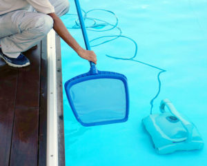 A person cleaning and maintaining a pool with a net and pool cleaner